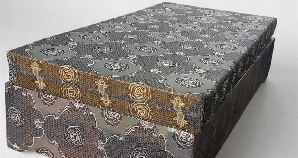 Single bed with a grey and gold rose-pattern cover on a matching base